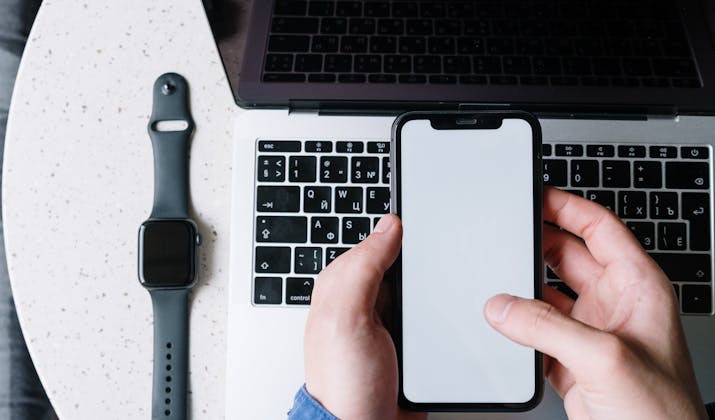 What Is The Apple Watch Walkie Talkie Range? 2 Hands holding iPhone above MacBook keyboard with Apple Watch beside laptop