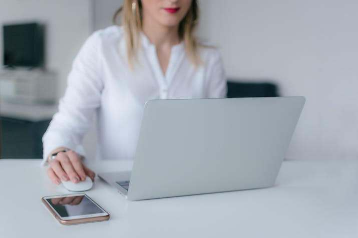 How To Easily Retrieve Your Apple ID Password From Mac Keychain 4 Person in a white shirt working on a silver laptop at a clean desk; a smartphone lies next to a wireless mouse