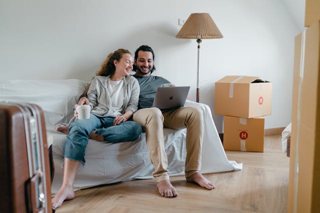 How To Connect MacBook to Sonos 2 Smiling couple relaxing on a sofa using a laptop in a new apartment with moving boxes.