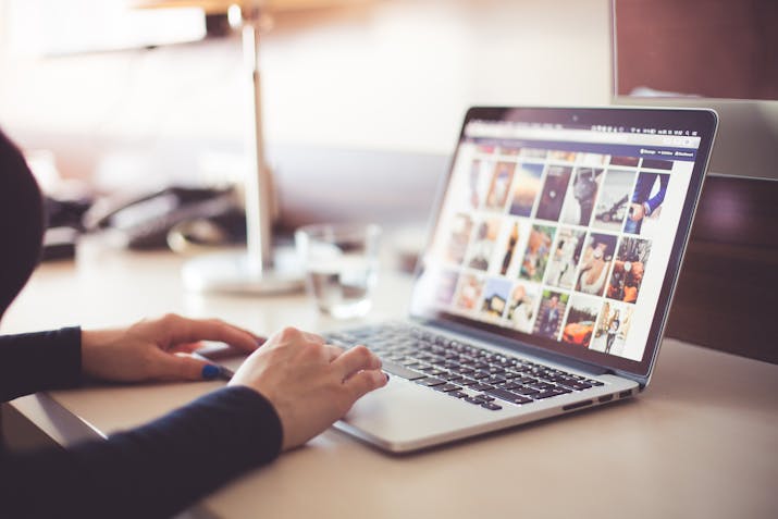 How To Easily Retrieve Your Apple ID Password From Mac Keychain 1 A person using a MacBook at a desk, browsing a grid of photos on a website; a glass of water and other desk items are blurred in the background