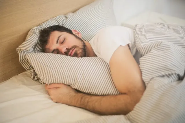 Man sleeping in bed under a striped duvet, restful sleep concept