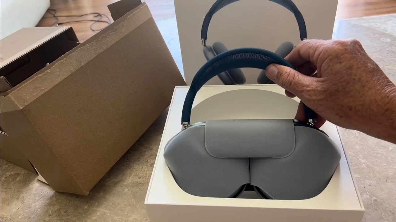 Person lifting blue Apple AirPods Max out of the retail box; headphones are inside the included gray Smart Case
