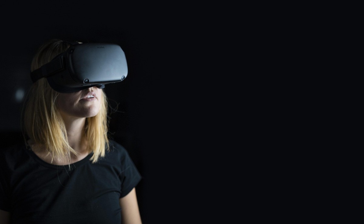 A woman in a dark room wearing a black oculus.